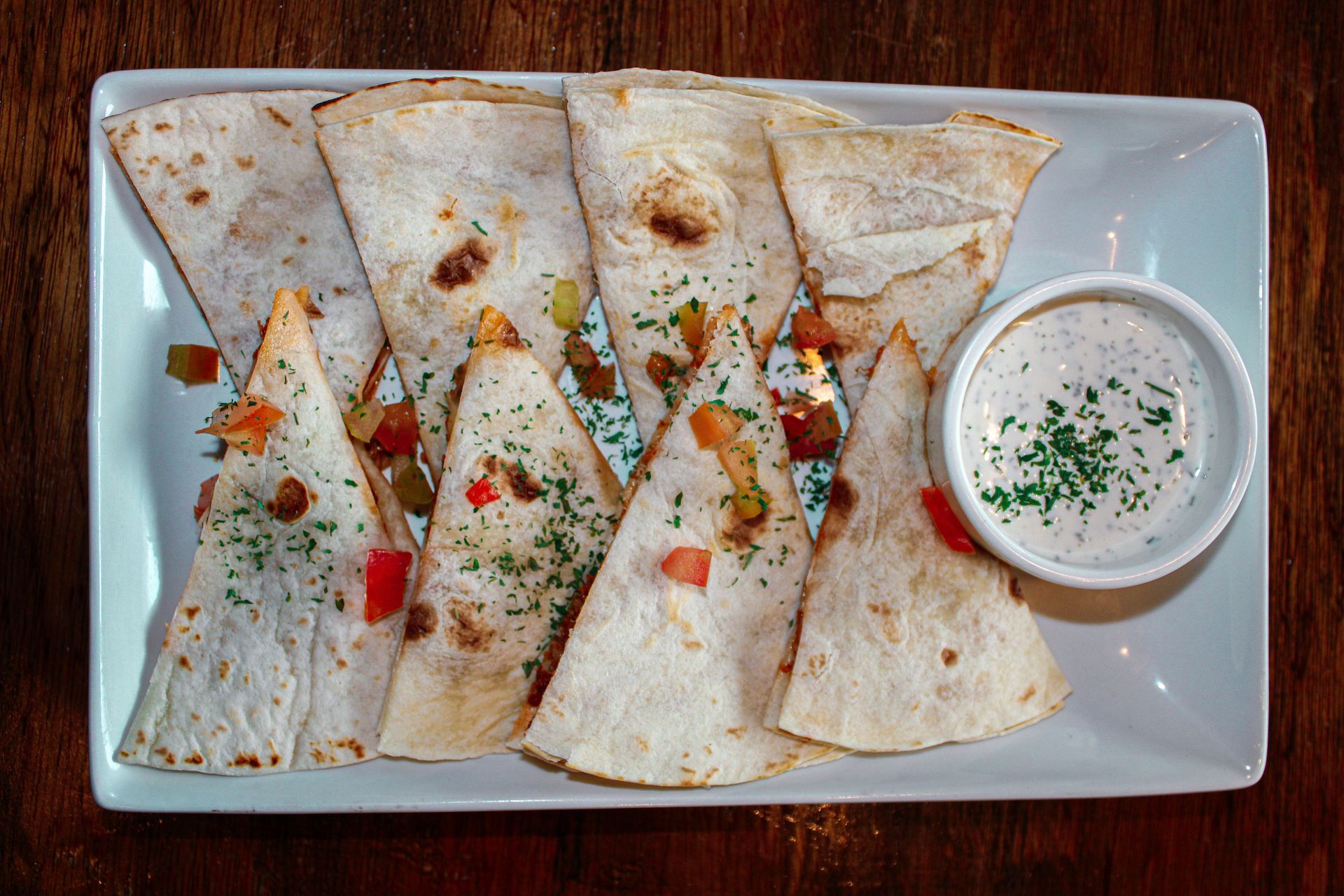 Mouthwatering cheese quesadillas served with fresh salsa and creamy dip on a white plate.